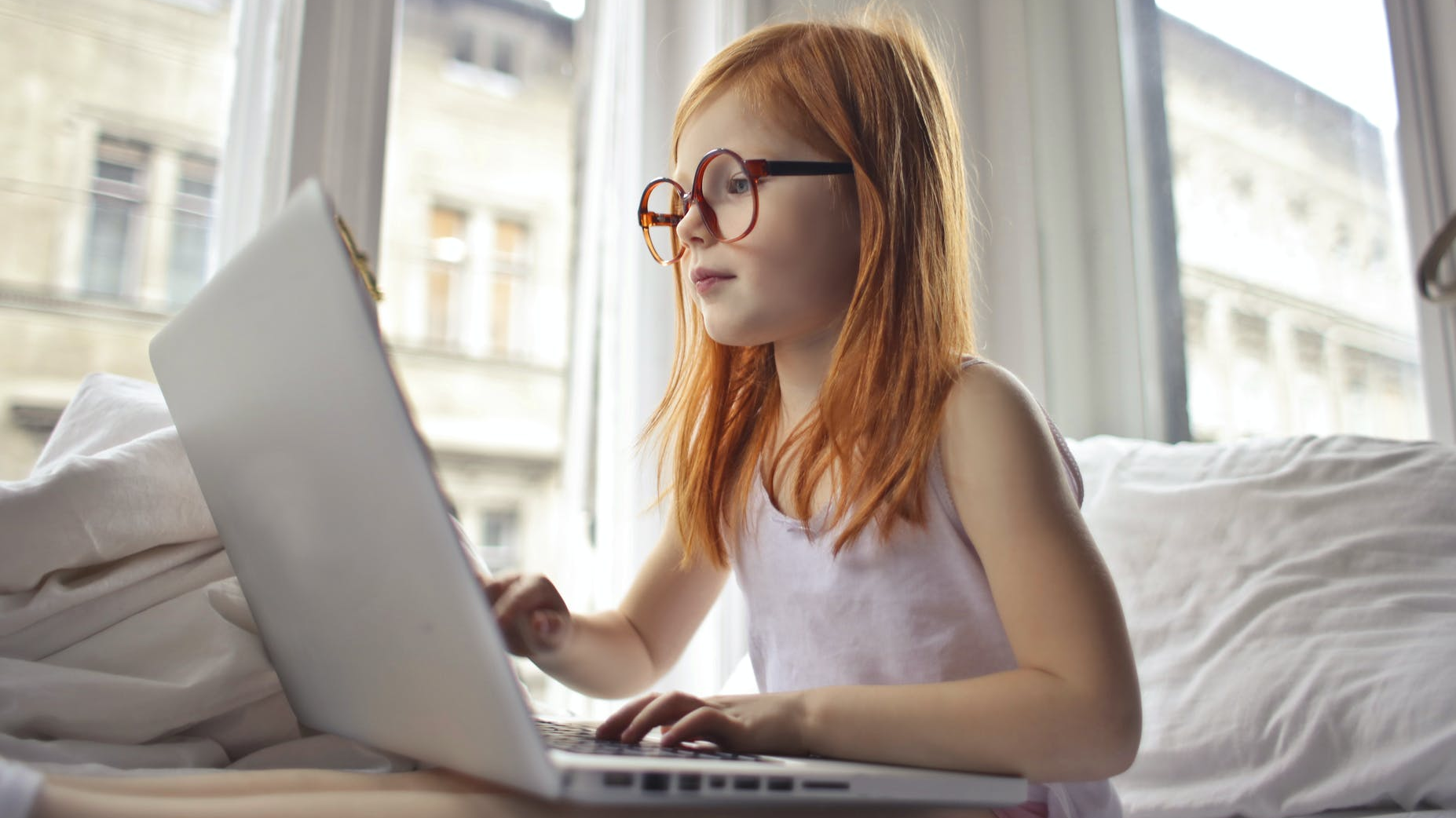 A photo of a young girl with long red hair and glasses using a laptop