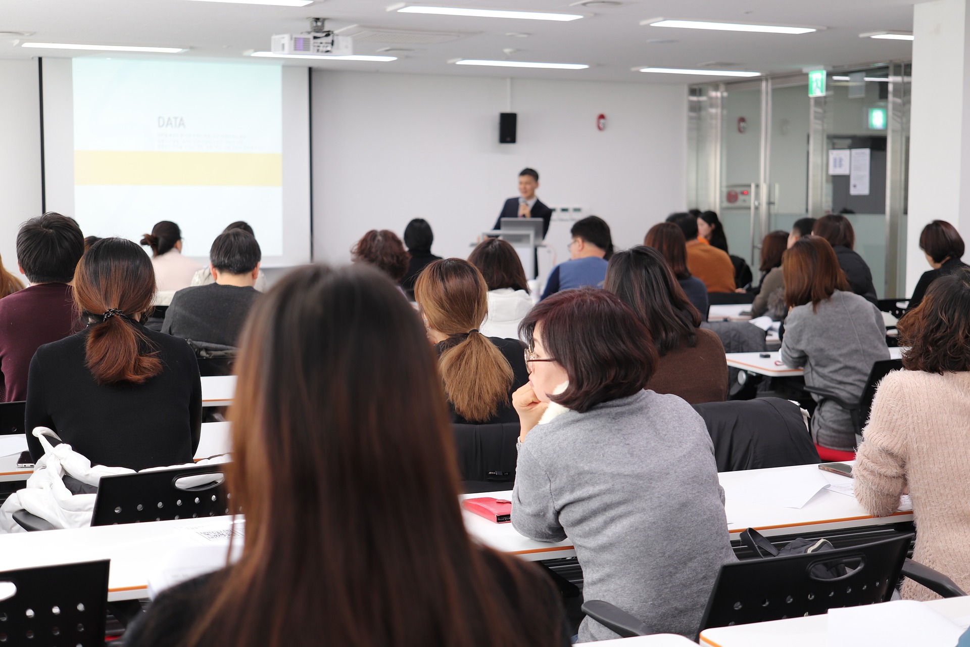 Photo of an audience watching a research seminar - the backs of their heads are visible and someone is presenting at the front of the room