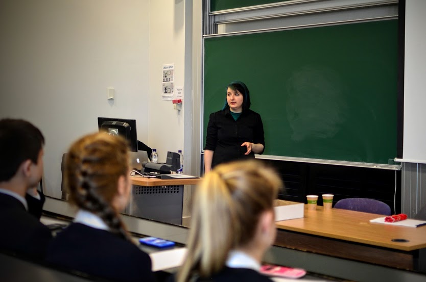 Photo of Katie Steckles presenting in front of a blackboard; some children are seated in the front row